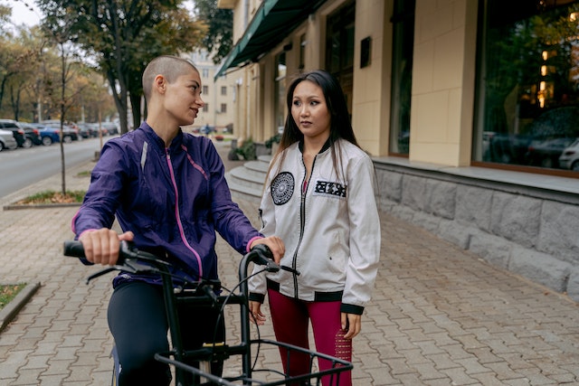 Person pushing a bike while talking to another person who is walking beside them in an empty street