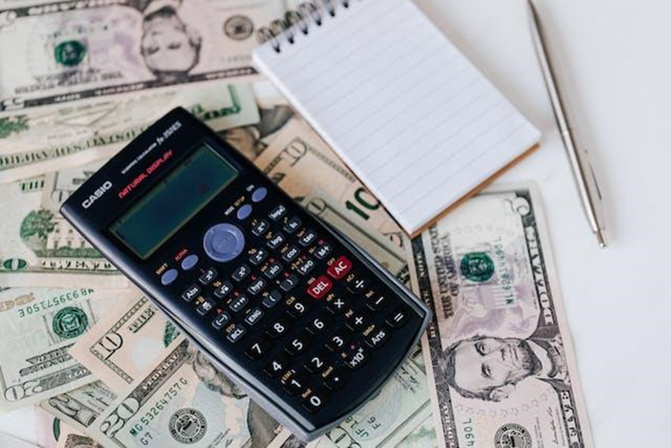 Calculator, notepad, pen, and banknotes on white table